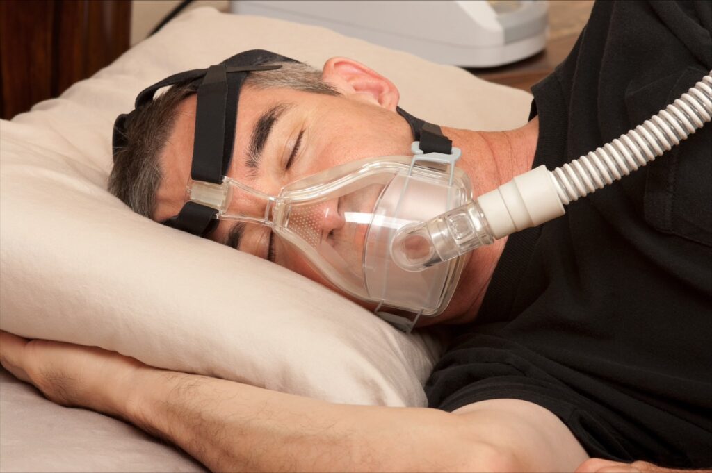 Man laying on his side with Sleep Apnea breathing device hooked up.