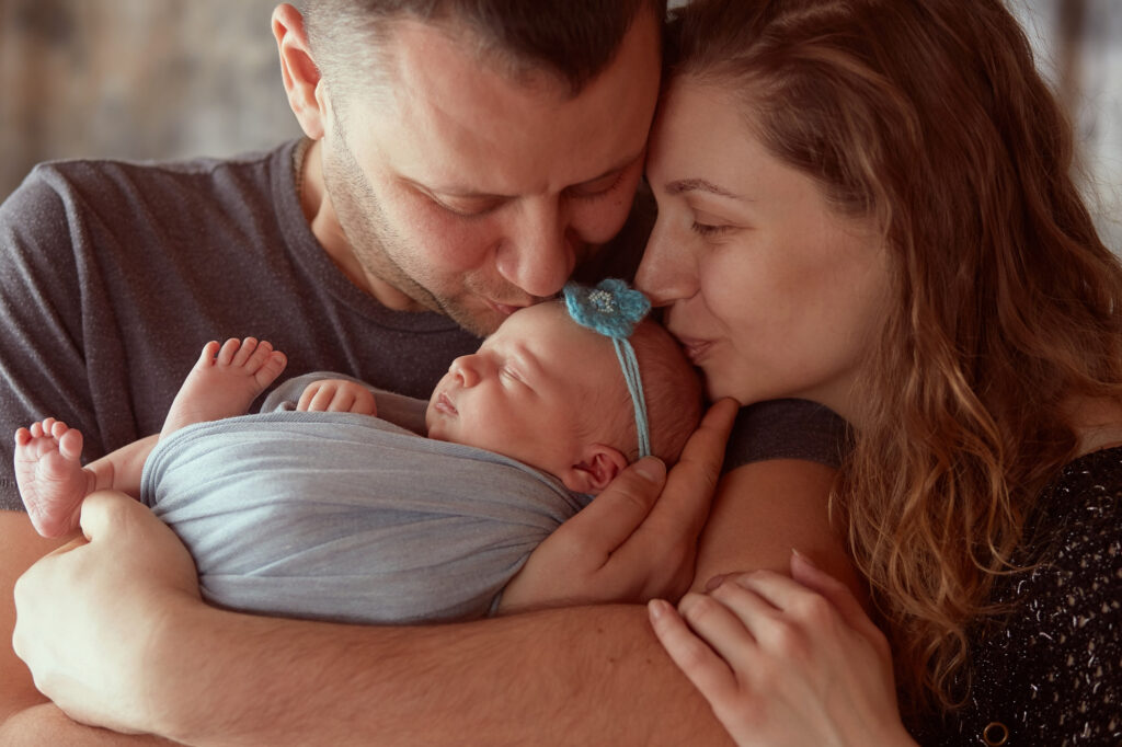 A couple holding a newborn baby and kissing the baby’s forehead