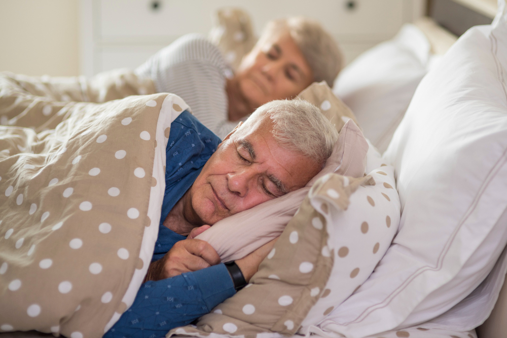 Two elderly couple sleeping in bed with the morning lights warming their bedroom in the early hours of the morning