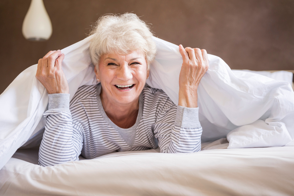 A happy elderly woman under the bed covers just after waking up from a deep and restful sleep in the morning