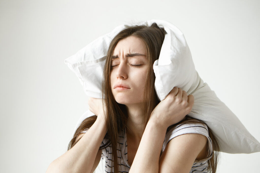 A young Girl with a pillow around her head and ears trying to catch some sleep
