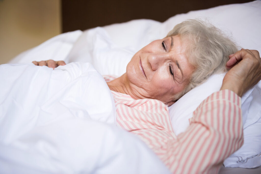 An elderly lady sleeping on a white bed with a smile on her face