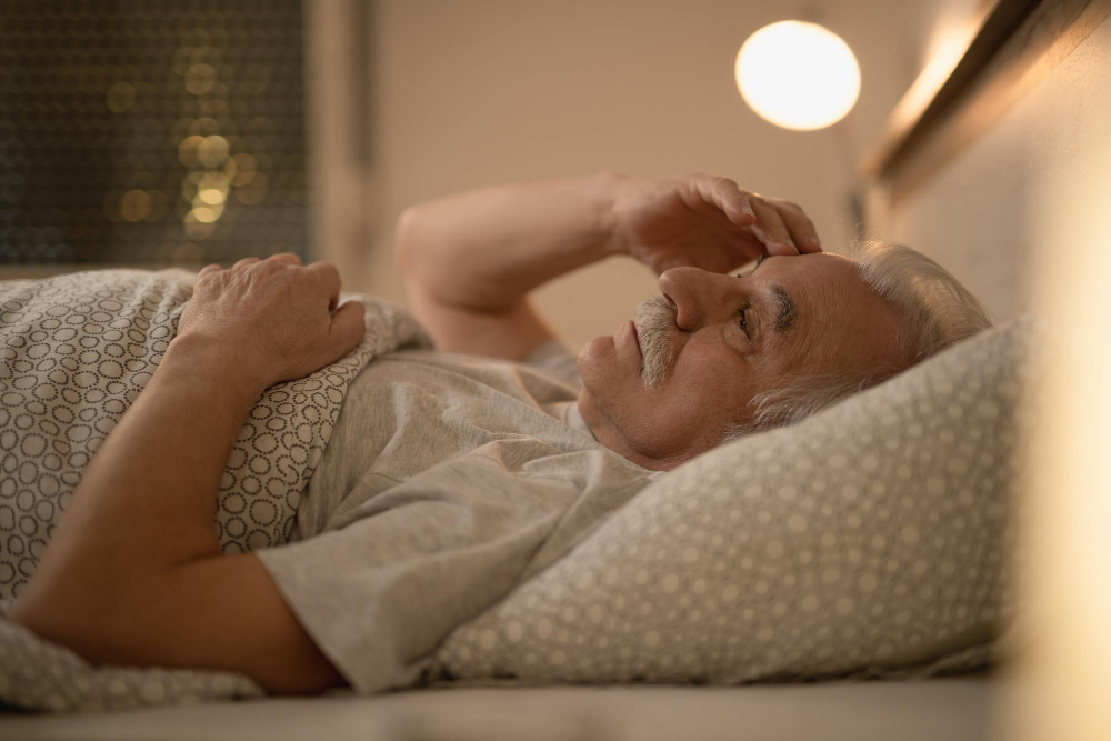 An elderly man lying in bed thinking with warm light around him worrying over lack of sleep