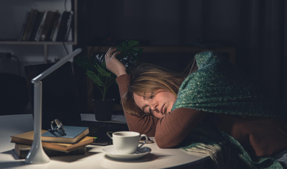 A tired young woman on a desk falling asleep with a coffee mug next to her