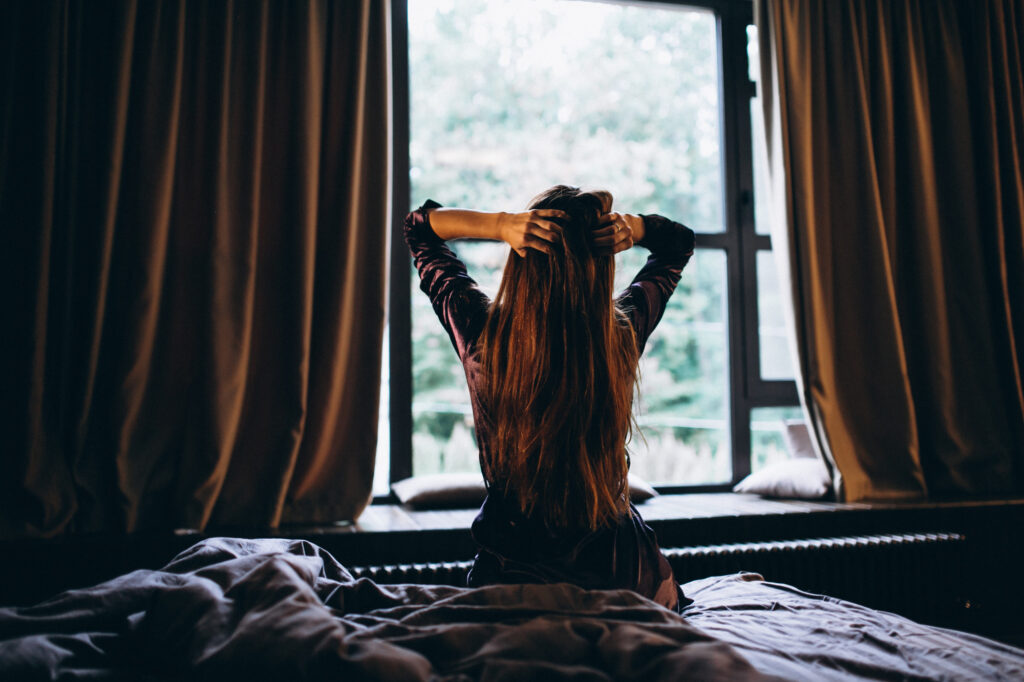 A young girl waking up to the day in a dark room with dark curtains drawn sightly open