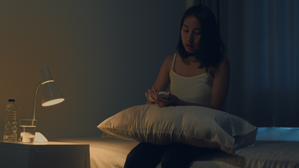 A young woman in a dark room with a pillow on her lap winding down for a restful sleep